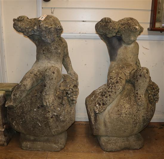 A pair of reconstituted stone Bacchanalian cherubs sitting on wine barrels H.94cm